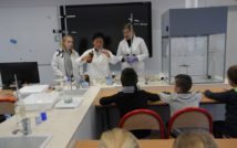 zdjęcie przedstawia klasę chemii w Liceum Ogólnokształcącym im. Mikołaja Kopernika. doł zdjęcia przedstawia siedzące tyłem dzieci. w centralnej górnej części zdjęcia stoją 2 uczennice wraz z nauczycielką chemii i wykonują eksperyment wykorzystując ciecz z butelki i probówkę