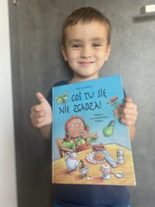 uśmiechnięty chłopiec trzyma książkę "Coś tu się nie zgadza"