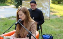 Siedząca w fotelu kobieta, przed nią mikrofon. Z tyłusiedzi mężczyzna, za nim plansza.
