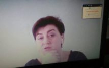 Kobieta prowadząca spotkanie online, w uchu ma słuchawkę, z tyłu ekran.