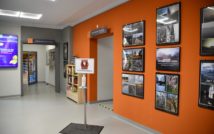 hol biblioteki, po prawej stronie ramy z konkursowymi zdjęciami, centralnie stanowisko do dezynfekcji rąk, po lewej monitor reklamowy