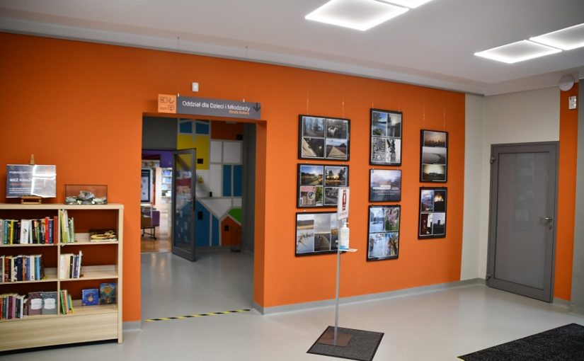hol biblioteki, po lewej półka z ksiazkami, po prawej ramy ze zdjęciami konkursowymi