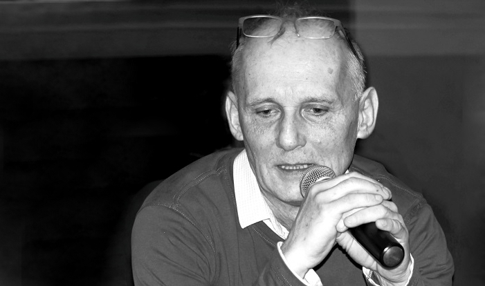 czarno-biała fotografia siedzącego mężczyzny z mikrofonem w ręce