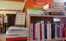 Fotografia regału z ksiażkami. Na książkach stoi czytnik