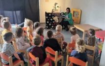 dzieci siedzą plecami na krzesłacch.Przed nimi pani nauczycielka czyta książkę.Za nią teatrzyk cieni.