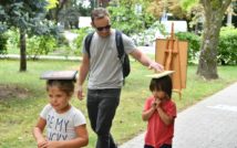 Trzy osoby na świeżym powietrzu: mężczyzna i dwoje dzieci. Dzieci niosą na głowach książki.
